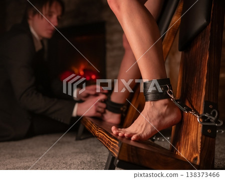 A man chains a woman's legs to a BDSM cross. 138373466