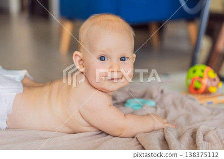 Baby lying on play mat learning to crawl and get on all fours. Infant practicing motor skills and development at home. Early childhood growth, milestones and active learning concept 138375112