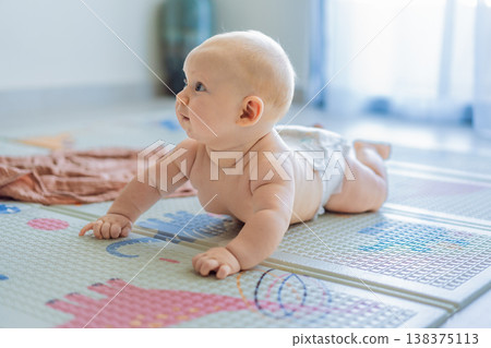 Baby lying on play mat learning to crawl and get on all fours. Infant practicing motor skills and development at home. Early childhood growth, milestones and active learning concept 138375113