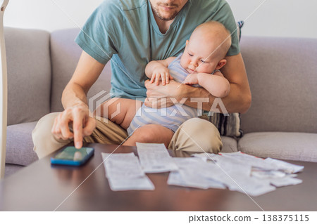 Father sitting on sofa holding baby while calculating monthly expenses with receipts at home. Stressed dad managing budget and childcare. Financial stress, parenthood and real life concept 138375115