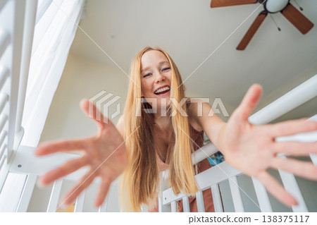 Mother looking into baby crib and playing with newborn at home. Loving mom bonding with infant, smiling and interacting. Parenting care, early childhood development and emotional connection concept 138375117