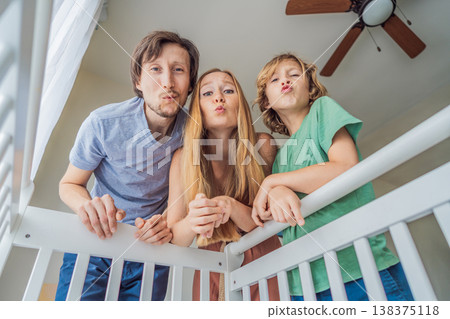 Parents and older brother looking into baby crib from infant point of view. Family smiling down at newborn with love and care. Sibling bonding, parenthood, childhood memory and connection concept Parents and older brother looking into baby crib from infant point of view. Family smiling down at newborn with love and care. Sibling bonding, parenthood, childhood memory and connection concept 138375118