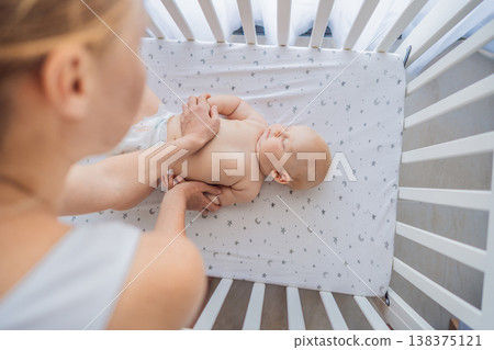 Mother gently placing sleeping baby into crib at home. Caring mom putting newborn to bed with tenderness and love. Bedtime routine, parenting care, early childhood and family bonding concept Mother gently placing sleeping baby into crib at home. Caring mom putting newborn to bed with tenderness and love. Bedtime routine, parenting care, early childhood and family bonding concept 138375121