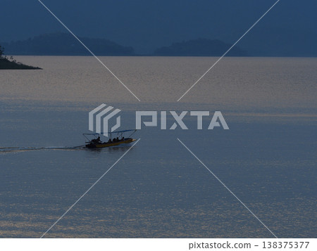 Lake boat dusk silhouette calm water mountain passenger boat moves across calm lake at dusk with peaceful twilight mood Lake boat dusk silhouette calm water mountain passenger boat moves across calm lake at dusk with peaceful twilight mood 138375377