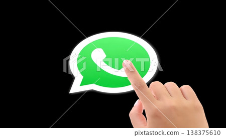 A human hand with a finger pointing directly at the iconic green WhatsApp messenger logo set against a dark black background, symbolizing digital communication, mobile technology A human hand with a finger pointing directly at the iconic green WhatsApp messenger logo set against a dark black background, symbolizing digital communication, mobile technology 138375610