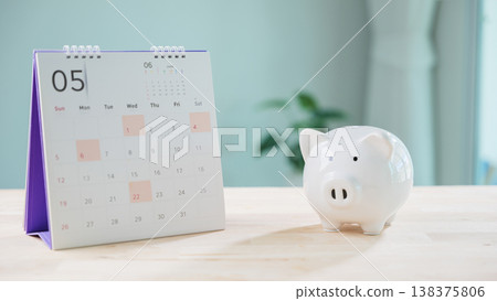 White ceramic piggy bank beside desk calendar helps save money, plan financial growth, manage retirement, insurance date, tax saving goals, organize budget on wooden table top 138375806