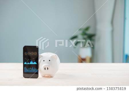 Digital savings mobile payment bank piggy phone payment save app shows online graphs, while black smartphone and white pig bank sit on wooden table for financial planning 138375819