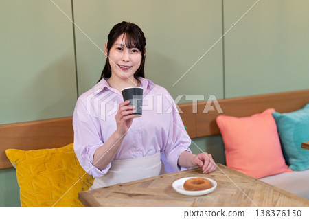 A smiling woman enjoying coffee and a donut at a cafe. A smiling woman enjoying coffee and a donut at a cafe. 138376150