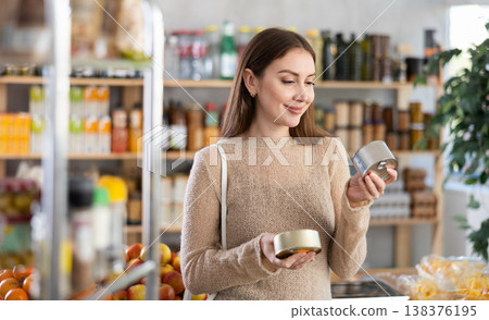 Young woman holding two tin cans of preserves in hands, choosing and shop around pate for sandwiches Young woman holding two tin cans of preserves in hands, choosing and shop around pate for sandwiches 138376195