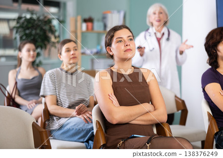 Diligent woman student with group of other interns listening lecture at lesson in university, doctor teacher in white coat in background Diligent woman student with group of other interns listening lecture at lesson in university, doctor teacher in white coat in background 138376249