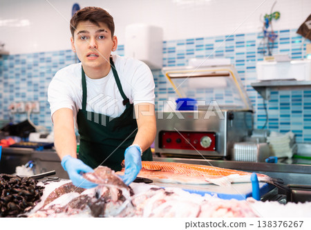 Positive seller in apron standing near counter offering fish striped red mullet 138376267