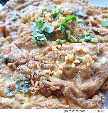 Close-up of a golden brown fried egg omelet served with aromatic garlic and green herbs. 138376365