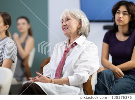 Focused mature lady with group of students different ages sitting on chairs and listening course in lecture hall Focused mature lady with group of students different ages sitting on chairs and listening course in lecture hall 138376376