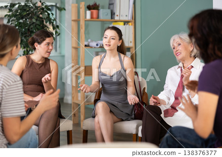 Focused female colleagues of different ages friendly talking while sitting in circle on chairs, psychological support in office Focused female colleagues of different ages friendly talking while sitting in circle on chairs, psychological support in office 138376377