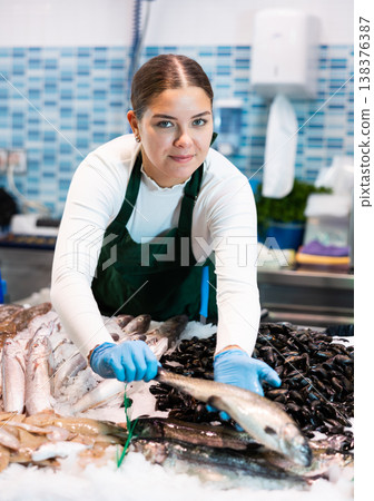 Positive saleswoman demonstrating trout in fish store Positive saleswoman demonstrating trout in fish store 138376387