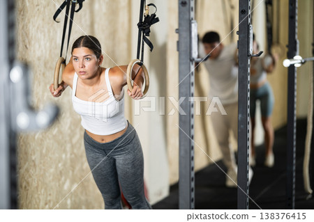 Girl trains on gymnastic rings in modern crossfit gym Girl trains on gymnastic rings in modern crossfit gym 138376415