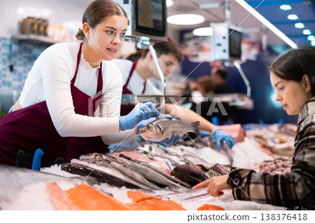 Woman seller of fish advises buyer to buy hake fresh fish 138376418