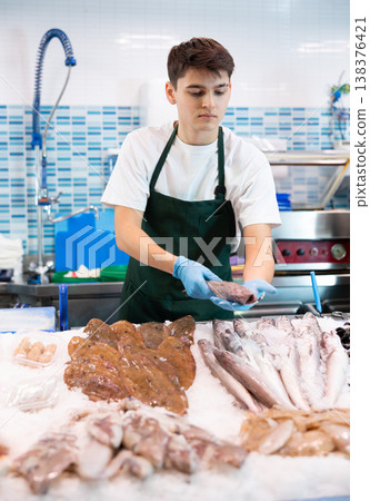Positive salesman demonstrating lucet fish in fish store 138376421