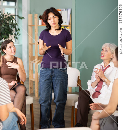 Confident young malaysian girl office worker standing near women sitting in circle talking and discussing ideas in office 138376506