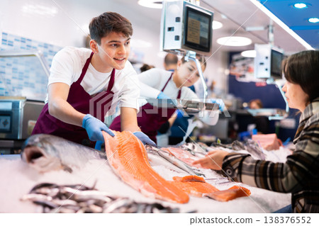 Portrait of man offering female customer fresh fish at seafood shop Portrait of man offering female customer fresh fish at seafood shop 138376552