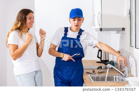Happy satisfied housewife checks operation of the water tap in the kitchen and thanks plumber 138376587