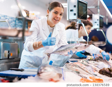 Positive saleswoman demonstrating bonito fish in fish store Positive saleswoman demonstrating bonito fish in fish store 138376589