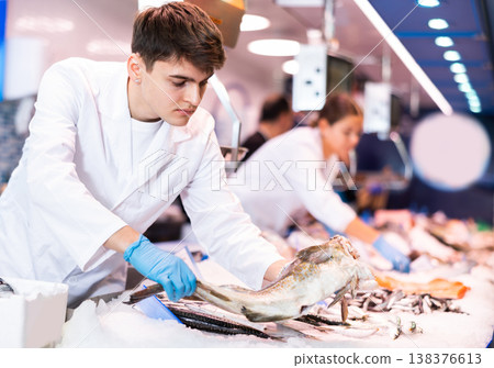Positive salesman demonstrating cod in fish store Positive salesman demonstrating cod in fish store 138376613