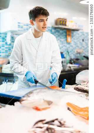 Seller with knife cut fish in supermarket near counter 138376660