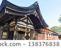 Traditional Japanese Shinto shrine architecture featuring a curved dark thatched roof and wooden structure with gold details. Clear blue sky background at a historical site in Osaka, Japan. 138376838