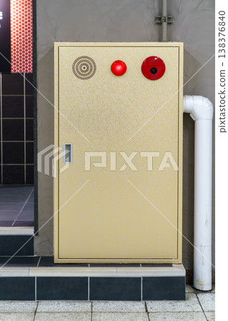 Industrial yellow fire hydrant cabinet with red emergency light and alarm button mounted on a textured wall. Professional safety and fire prevention equipment in a commercial building setting. Industrial yellow fire hydrant cabinet with red emergency light and alarm button mounted on a textured wall. Professional safety and fire prevention equipment in a commercial building setting. 138376840