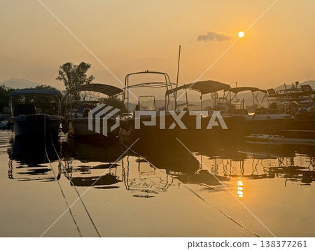 Boats docked at sunset with warm golden light reflecting on the calm water surface 138377261