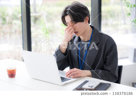 A scene depicting a young employee holding their eyes due to work fatigue, highlighting stress and poor health; a business image of eye strain and eye fatigue. 138378186