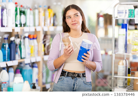 Girl selects and purchases paper cups in the household goods section of supermarket Girl selects and purchases paper cups in the household goods section of supermarket 138378446