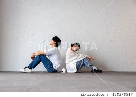 A young man and woman are sitting back-to-back with a house-shaped ornament in the middle, deep in thought and troubled. 138378517