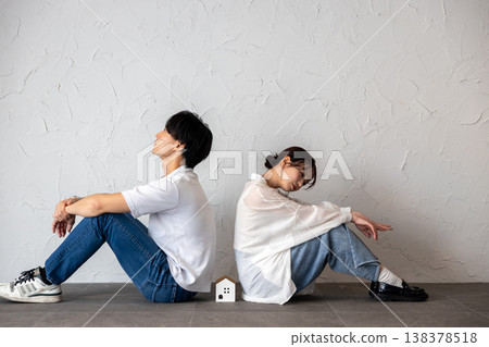 一對年輕男女背靠背坐著，中間放著一個房子形狀的裝飾品，他們若有所思，心事重重。 138378518