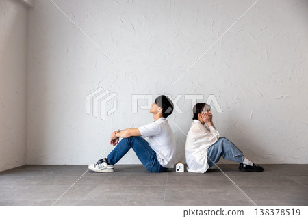 A young man and woman are sitting back-to-back with a house-shaped ornament in the middle, deep in thought and troubled. 138378519