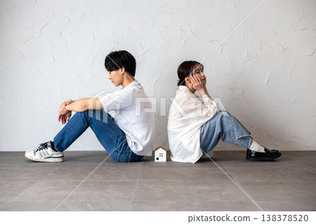 A young man and woman are sitting back-to-back with a house-shaped ornament in the middle, deep in thought and troubled. 138378520