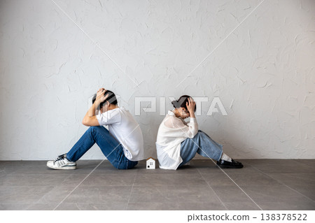 一對年輕男女背靠背坐著，中間放著一個房子形狀的裝飾品，他們若有所思，心事重重。 138378522