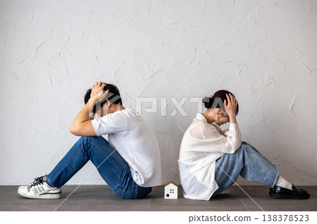 A young man and woman are sitting back-to-back with a house-shaped ornament in the middle, deep in thought and troubled. 138378523