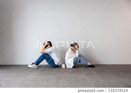 A young man and woman are sitting back-to-back with a house-shaped ornament in the middle, deep in thought and troubled. 138378524