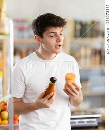 Male buyer carefully reads labels on sauce - chooses the best product in supermarket 138378585