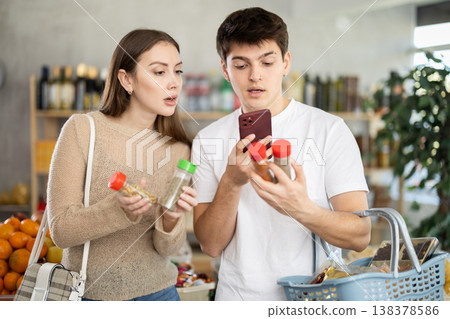 Positive young couple chooses and buys delicious spices and seasonings together in market and scan QR code Positive young couple chooses and buys delicious spices and seasonings together in market and scan QR code 138378586