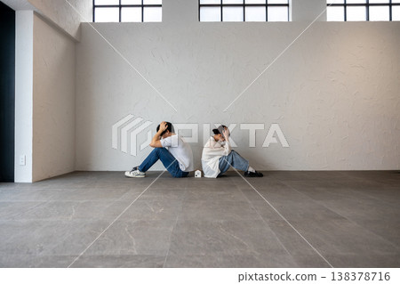 A young man and woman are sitting back-to-back with a house-shaped ornament in the middle, their heads in their hands, deep in thought and troubled. 138378716