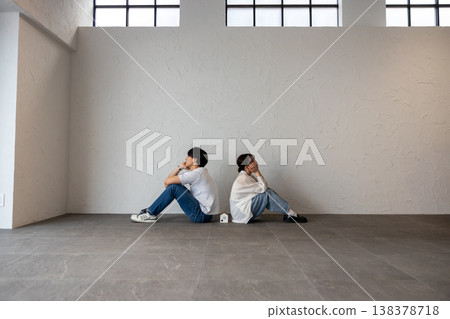 A young man and woman are sitting back-to-back with a house-shaped ornament in the middle, deep in thought and troubled. 138378718