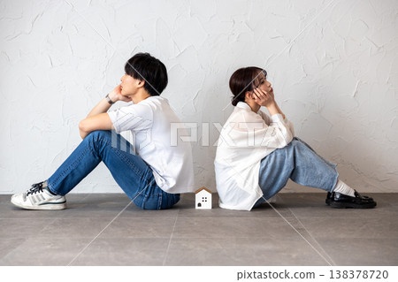 A young man and woman are sitting back-to-back with a house-shaped ornament in the middle, deep in thought and troubled. 138378720