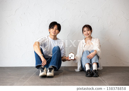 一對年輕夫婦，一男一女，正坐在牆邊擺弄著他們自製的手工藝品。 138378858