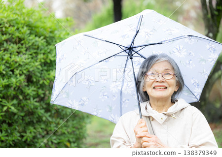 A close-up of a calm, healthy, and active senior enjoying a walk in the rainy season with an umbrella. 138379349