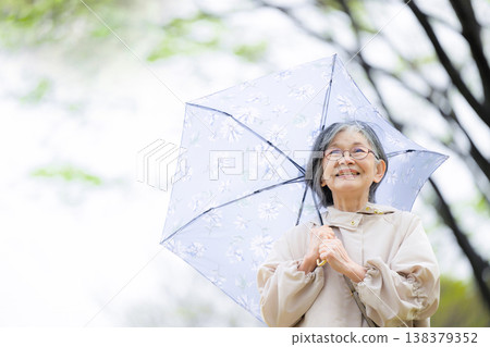 A close-up of a calm, healthy, and active senior enjoying a walk in the rainy season with an umbrella. 138379352