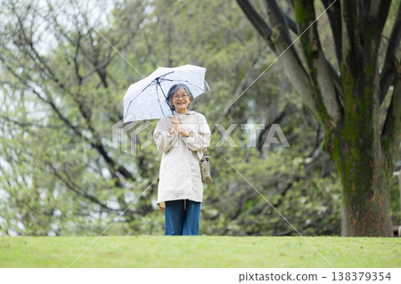 一位平靜、健康、活躍的老婦人在雨季撐著傘散步。 138379354