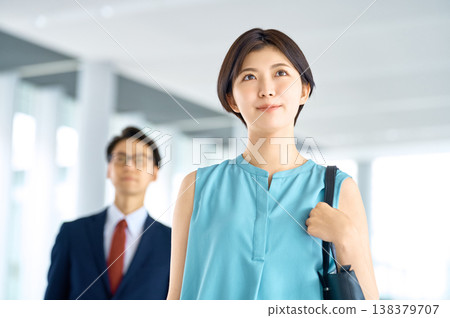 一位在辦公區工作的女商人面帶笑容，眺望著未來，她的同事站在她身後。 138379707